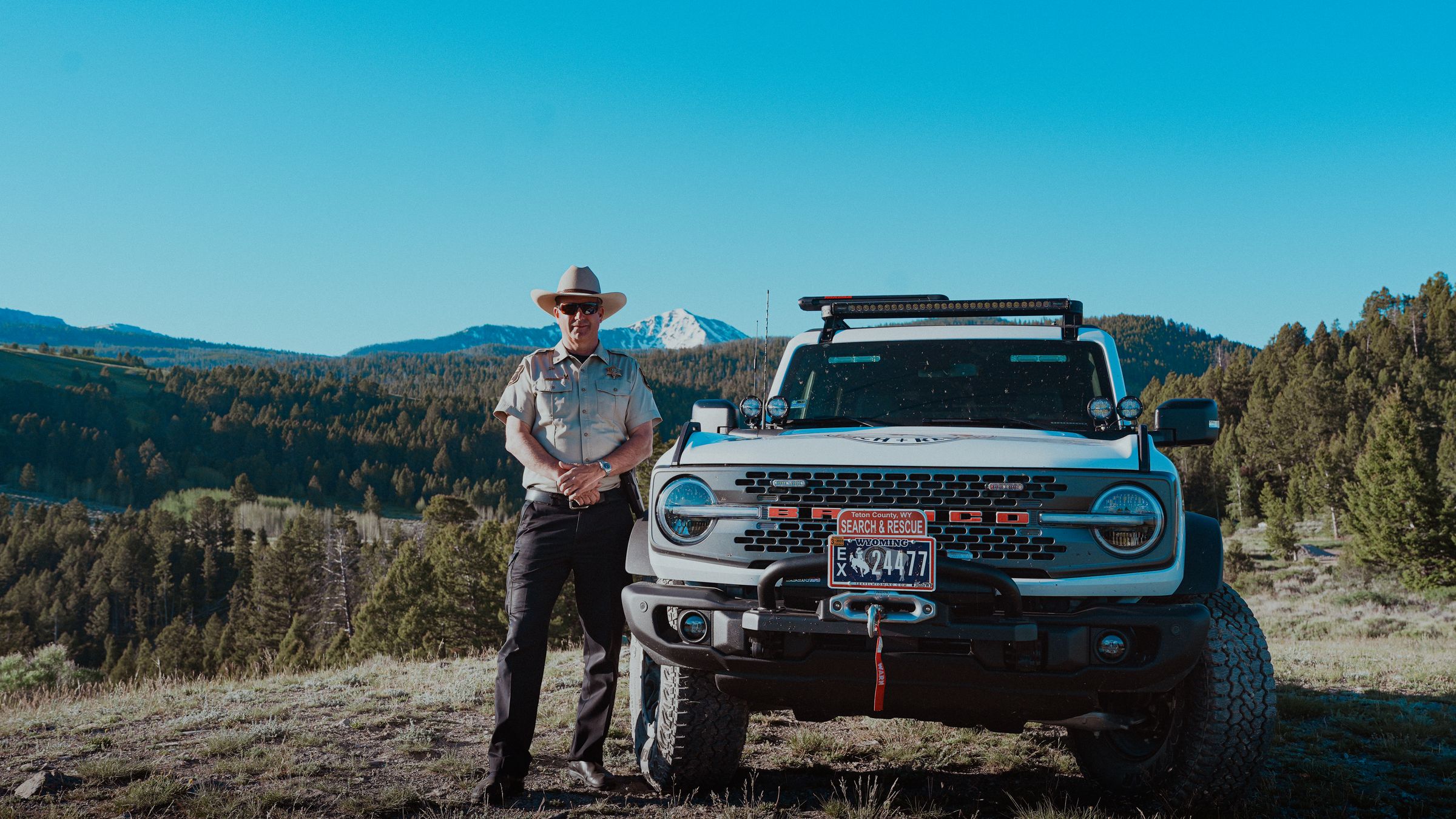 Sheriff Matt Carr standing beside the Teton County Search and Rescue Bronco with the mountains behind him