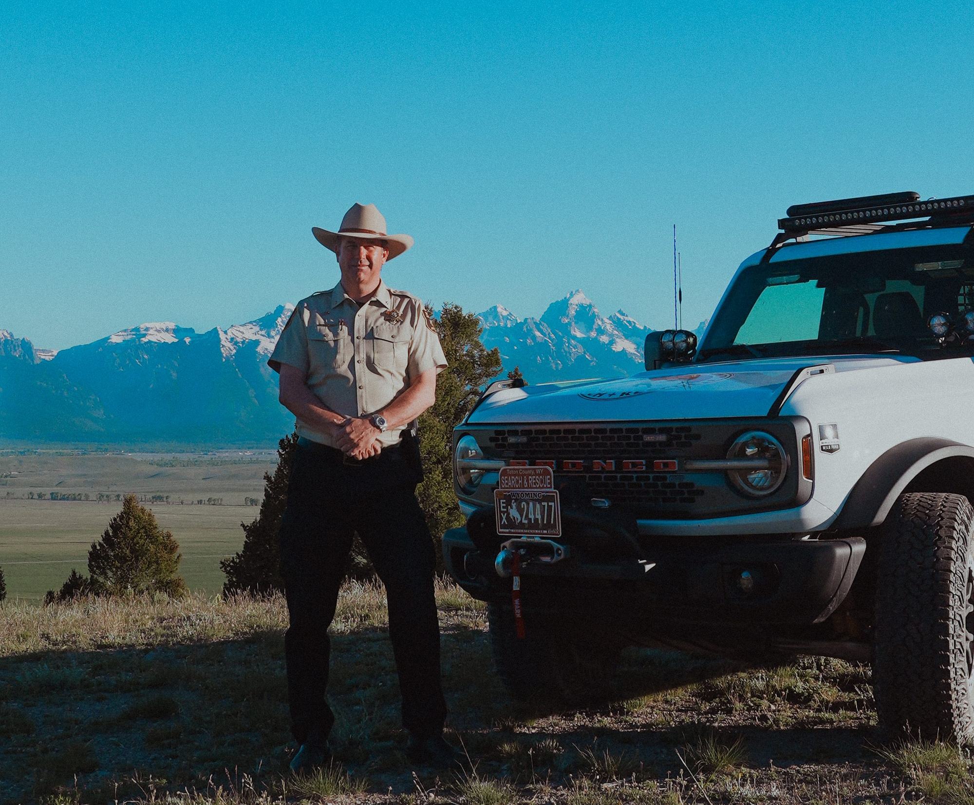 Sheriff Matt Carr standing beside the Teton County Search and Rescue Bronco with the mountains behind him